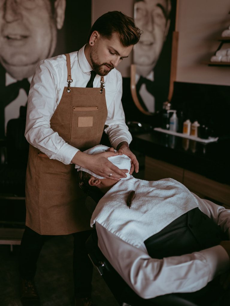 Blanche Maconald Graduate Cody Dunbar provides a hot shave service on a client at Edmonton's Black Forest Barbershop