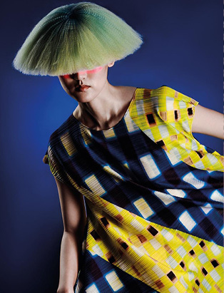 editorial shot of a model in yellow and blue dress, with a yellowish green hairstyle, covering her eyes