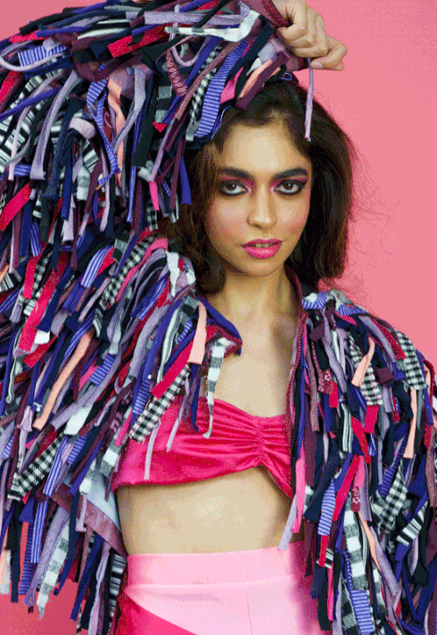 a female model wearing Fashion Design Graduate Jasper Cote's collection with multicoloured fabric strip fringe bolero jacket with burgundy vinyl belt closures