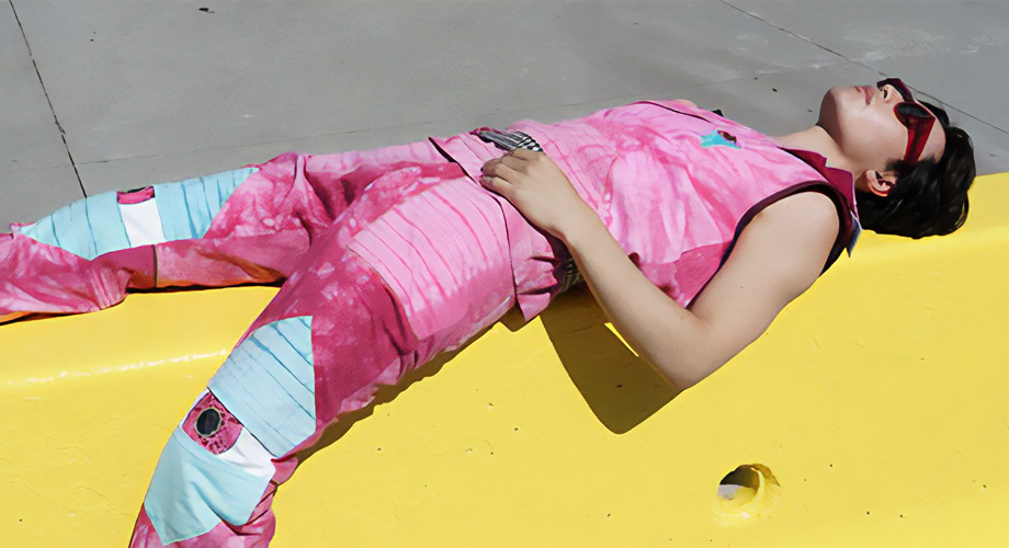 a male model laying down on a yellow structure with Fashion Design Graduate, Jasper Cote's garment