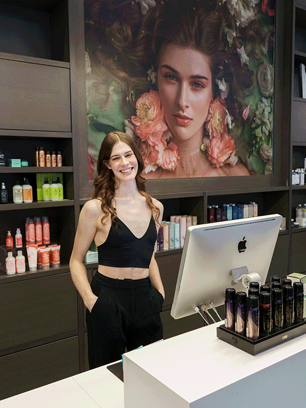 CurliQue Beauty Q-Talent Leader Isabelle standing behind an iMac. and holding eyeshadow palettes