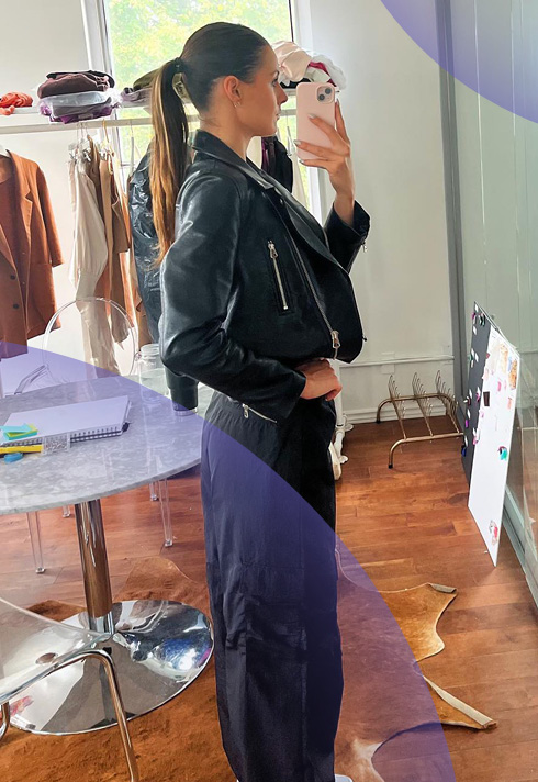 Right sided selfie by Anonda Hoppner, ALDO's Associate Buyer, standing in front of a marble table wearing a black leather jacket