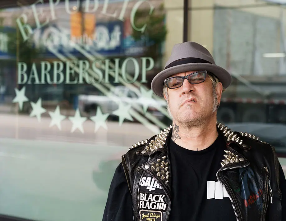 Ash, wearing a grey fedora hat, standing in front of his barber shop, Republic of East Vancouver