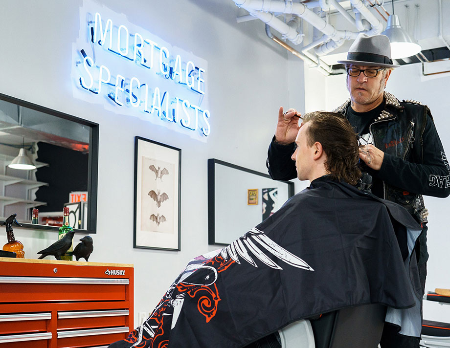 Ash, wearing a grey fedoras hat, cutting a customer's hair in his Republic of East Vancouver barber shop