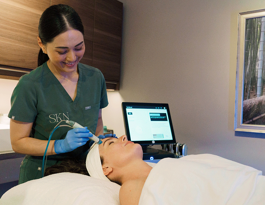 Laser esthetics technician Jackie performing HydraFacial on a female client, wearing a spa white robe