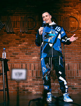 Comedian Joey Avery standing on the stage wearing San Jose Sharks rework tracksuit
