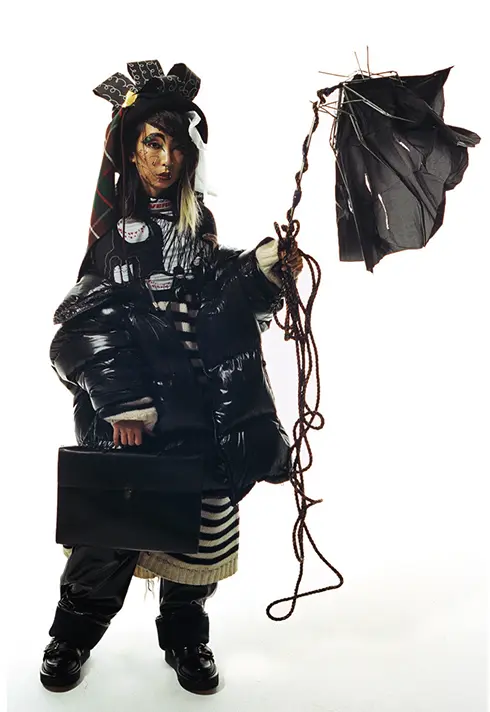 Full body shot of a model wearing black holding a black broken umbrella.