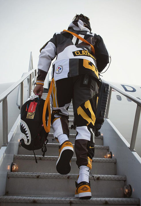 A back shot of Chase Claypool wearing a custom tracksuit for SNF at the airport with his black suitcase