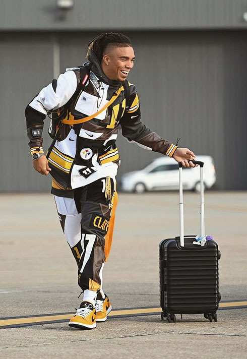 Chase Claypool wearing a custom tracksuit for SNF at the airport with his black suitcase