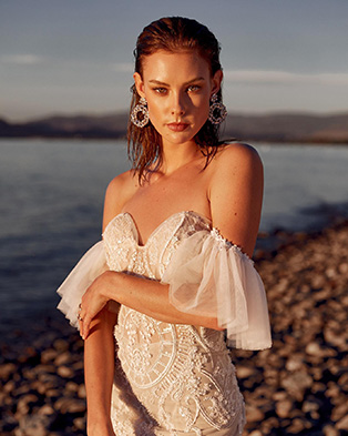A model wearing hair back, with silver round statement earrings posting near coast during golden hours 