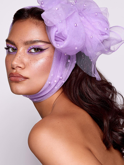 A model wearing purple bow on her hair with white pearls and purple eyeliner.