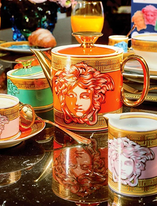 Product shot of Versace medusa orange amplified tea pot, and pink medusa amplified espresso cup & saucer

