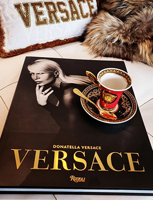 A high angle shot of the book Versace By Donatella Versace, with a Versace medusa red coffee set