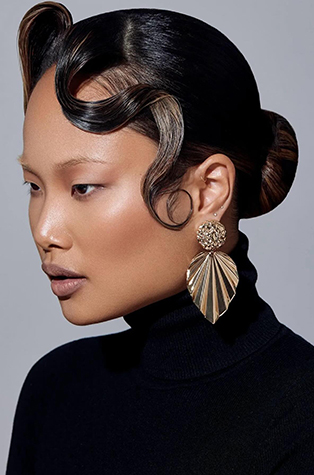 An asian model with light makeup wearing a black turtle neck and a silver leaf design earrings.