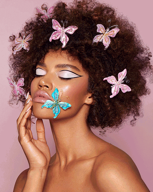 A Black female model with afro wearing pink butterflies on her hair, and light pink eyeshadows.